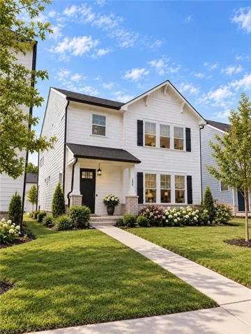White siding exterior with black shutters, covered porch with brick columns, front entry door with transom window, and a concrete walkway