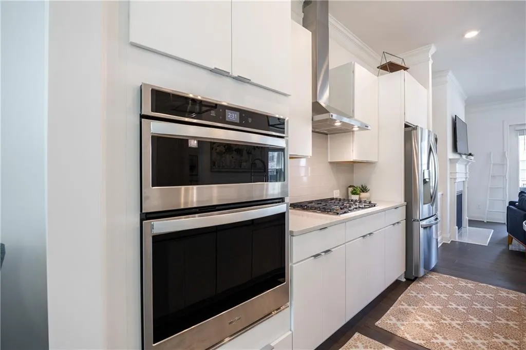 Kitchen with stainless steel appliances, crown molding, white cabinetry, dark wood-style floors, and decorative backsplash