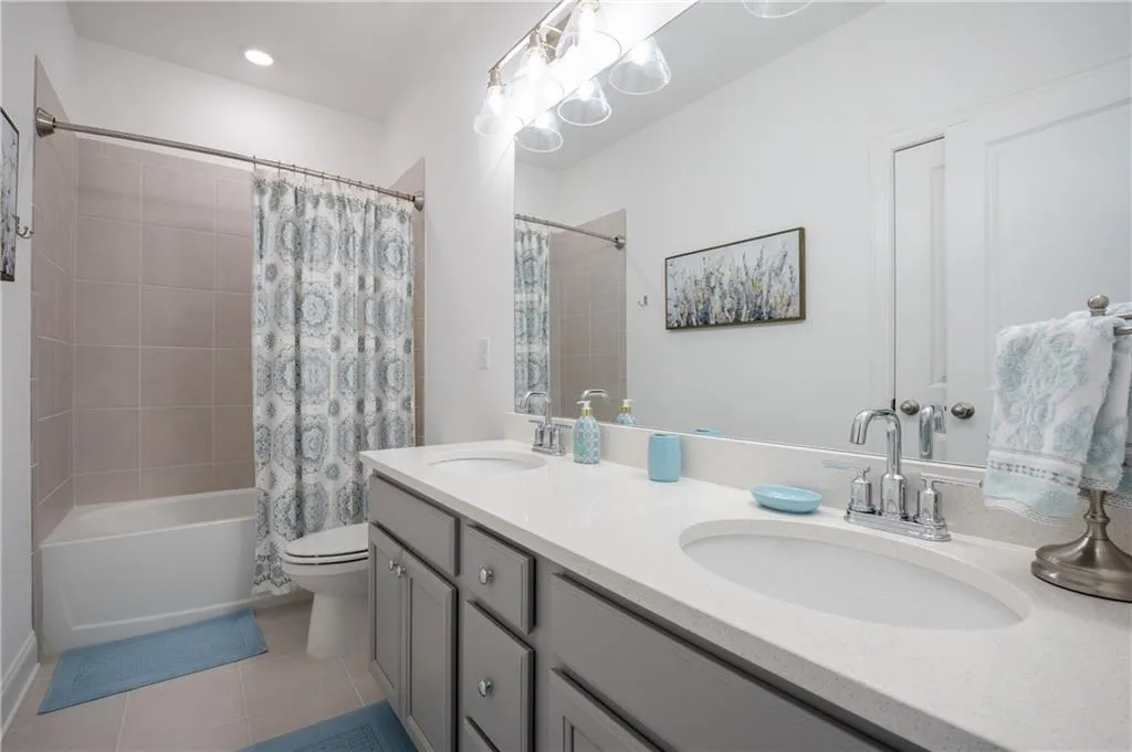 Bathroom with shower / bathtub combination with curtain, light tile patterned flooring, and double vanity