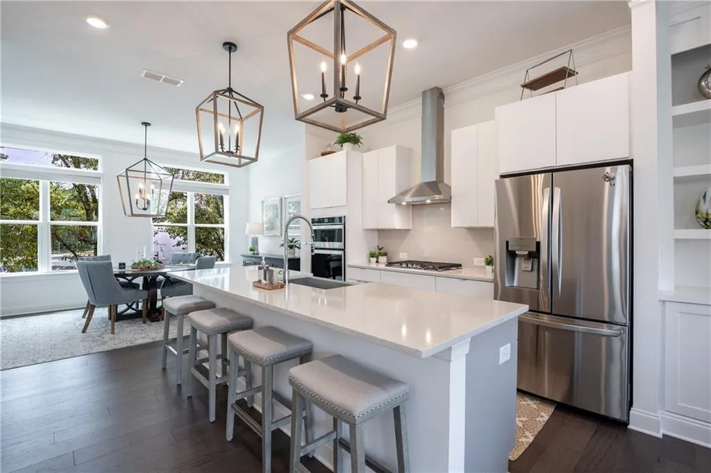 Kitchen featuring stainless steel appliances, a center island with sink, tasteful backsplash, hanging light fixtures, and white cabinets