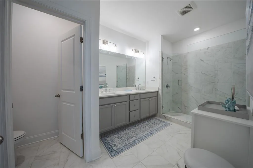 Bathroom featuring light marble finish floors, double vanity, a marble finish shower, and recessed lighting