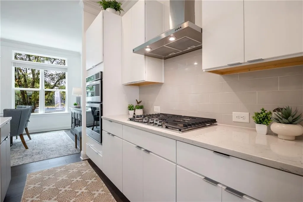 Kitchen with wall chimney exhaust hood, white cabinets, light stone counters, decorative backsplash, and crown molding
