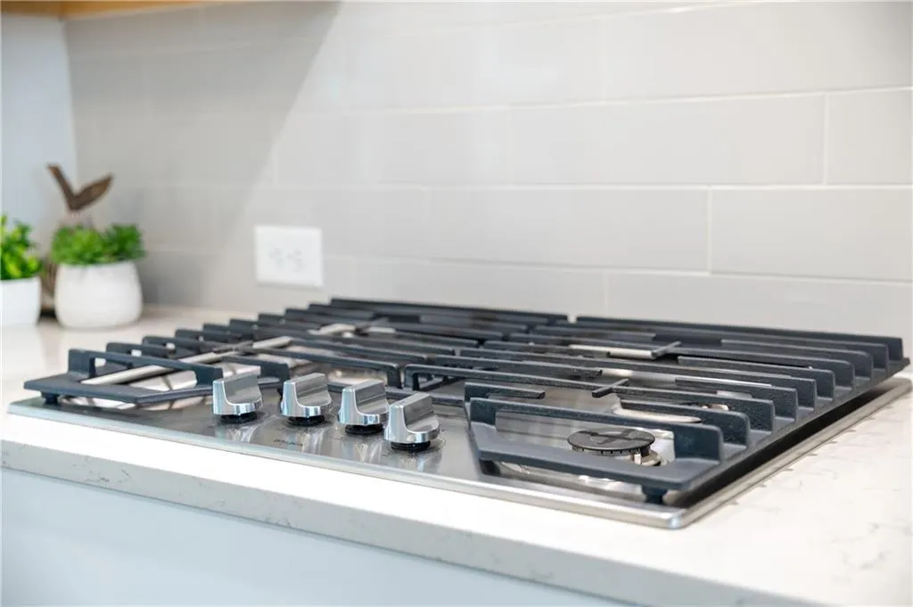 Kitchen view of stainless steel gas cooktop, decorative backsplash, and light stone counters