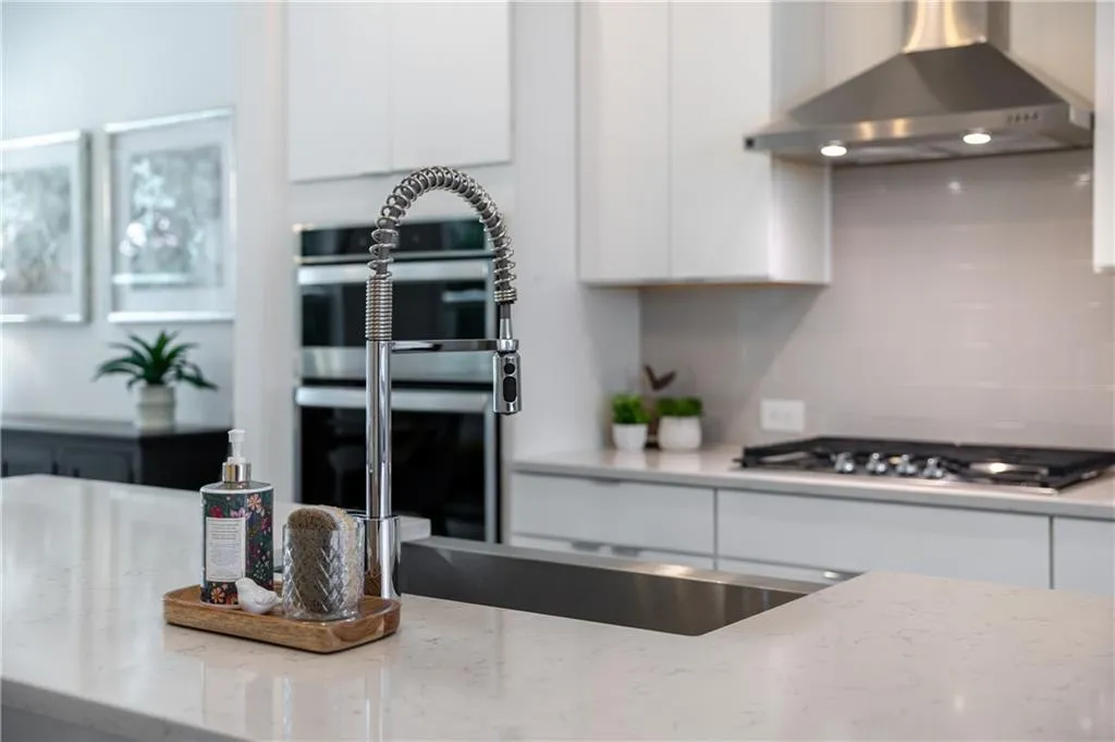 Kitchen featuring white cabinetry, wall chimney range hood, tasteful backsplash, and light stone countertops