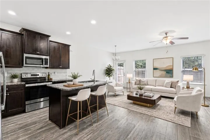 Virtually Staged - Open-concept living area featuring wood-finish flooring, a kitchen island with seating, stainless steel appliances, dark wood cabinetry, and recessed lighting