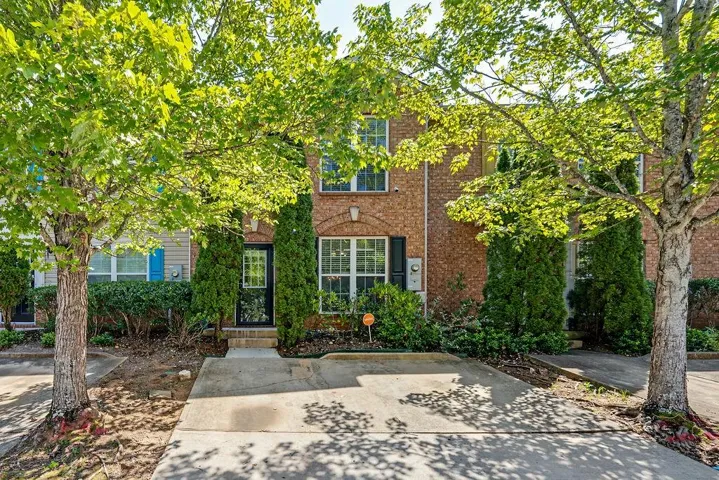 Brick exterior with a covered entry, mature trees, and a concrete driveway