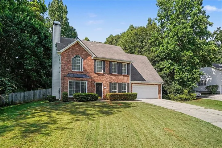 Brick exterior with dark shutters, arched window detail, two-car garage, established front landscaping, and a manicured lawn