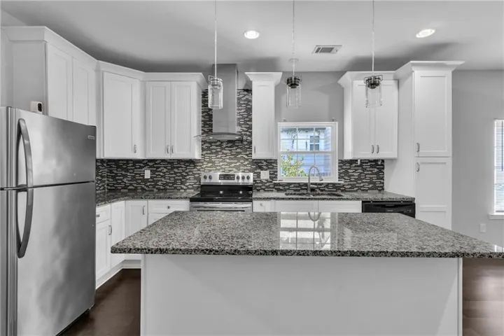 Modern kitchen featuring white cabinetry, granite countertops, a tile backsplash, stainless steel appliances, and dark wood-finish flooring