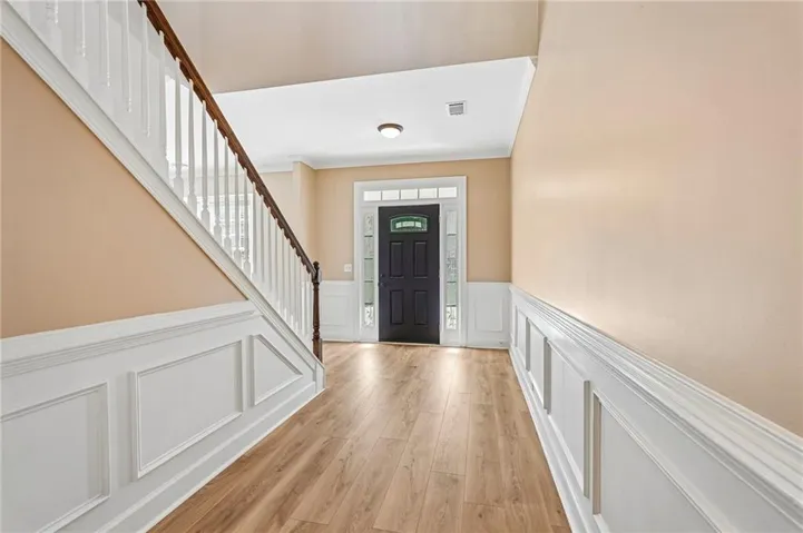 Entryway featuring wood-finish flooring, wainscoting, a staircase with white spindles and a dark wood handrail, and a dark paneled front door with decorative glass inserts