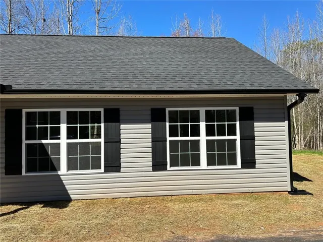 Gray shingled roof, light gray horizontal siding, black exterior shutters, white grid windows, and black gutters