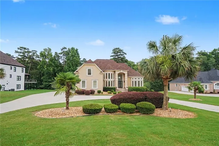 Stucco exterior residence featuring a curved driveway, mature palm trees, manicured shrubs, and a well-maintained lawn