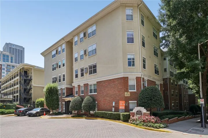 Multi-story building featuring a brick and stucco exterior, multiple windows, and a paved entrance with landscaping