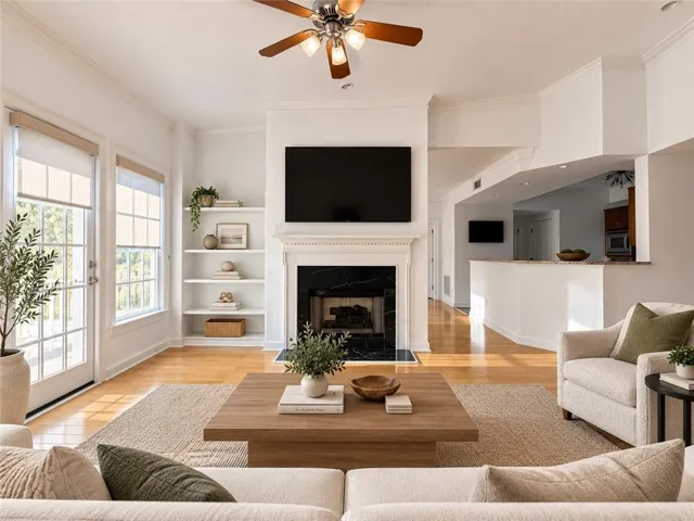Hardwood-style flooring throughout, prominent fireplace with a black surround, built-in shelving, two sets of French doors, and a ceiling fan