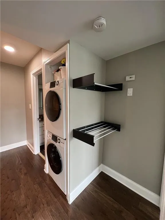 Laundry room with dark wood-type flooring and stacked washer and clothes dryer