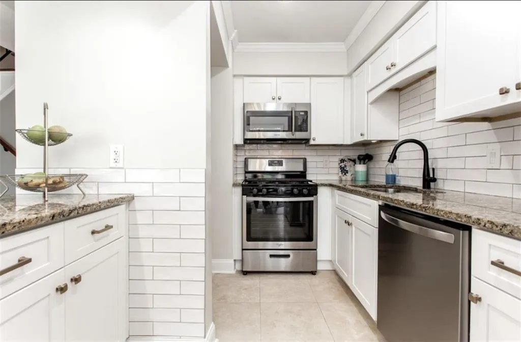 Kitchen with sink, stainless steel appliances, white cabinetry, and stone countertops