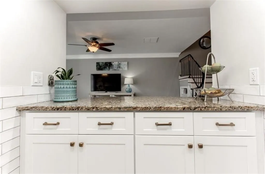 Kitchen with ceiling fan, kitchen peninsula, white cabinetry, and light stone countertops