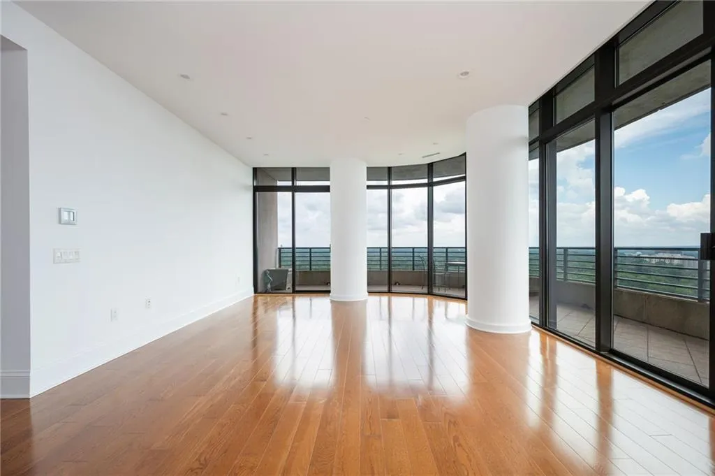 Expansive corner living space showcasing gleaming wood-finish flooring, floor-to-ceiling windows with black-framed glass panels, and panoramic vistas of the surrounding landscape