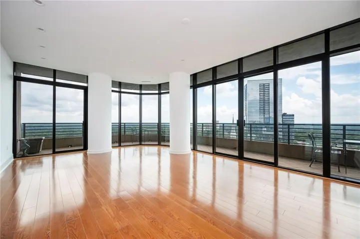 Expansive corner residence showcasing floor-to-ceiling black-framed glass walls, gleaming wood-finish flooring throughout, and panoramic cityscape vistas