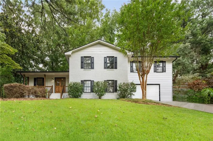 View of front of house featuring an attached garage, a front lawn, and view of scattered trees