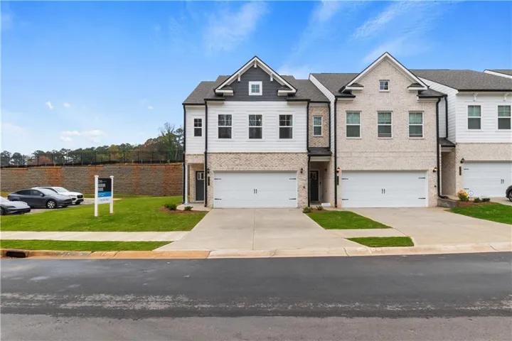 Modern townhome exterior featuring a two-car garage, brick facade, white siding, and a gabled roofline