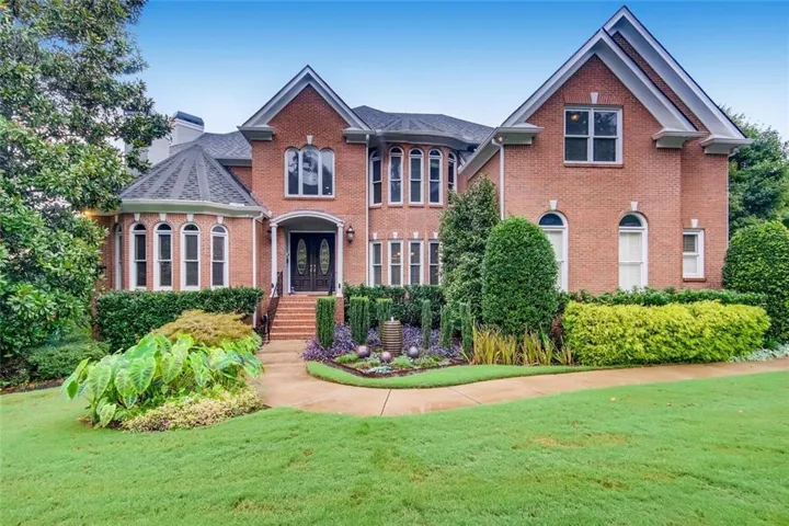 Brick exterior with a prominent gabled roofline, arched windows, a grand double-door entry, and detailed landscaping