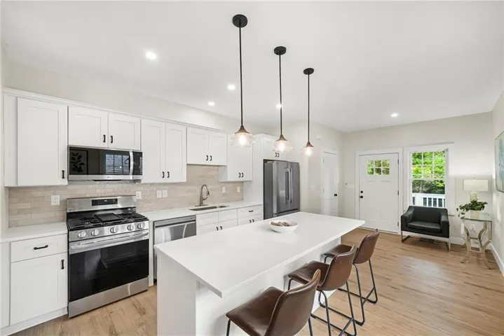Kitchen featuring white shaker cabinetry, stainless steel appliances, a center island with pendant lighting, light-toned wood-finish flooring, and a subway tile backsplash
