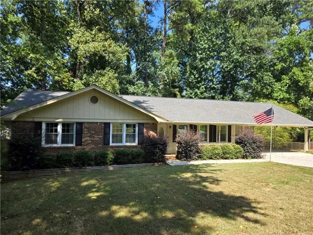 Brick exterior with a gabled roofline, front porch, mature landscaping, and an attached carport