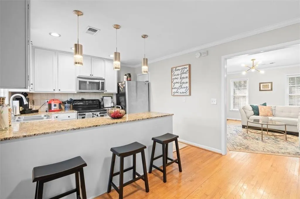 Kitchen with a breakfast bar area, light stone counters, backsplash, light wood finished floors, and stainless steel appliances