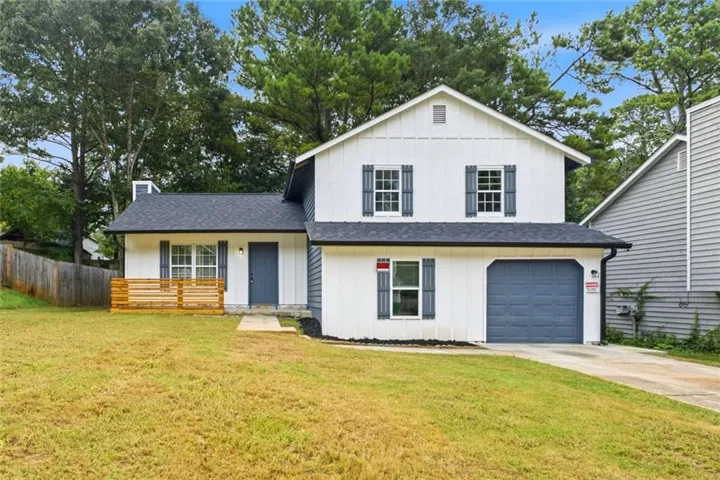 Two-story exterior featuring white vertical siding, a dark gray shingle roof, a two-car garage with a dark gray door, dark gray window shutters, and a front porch with a wooden railing