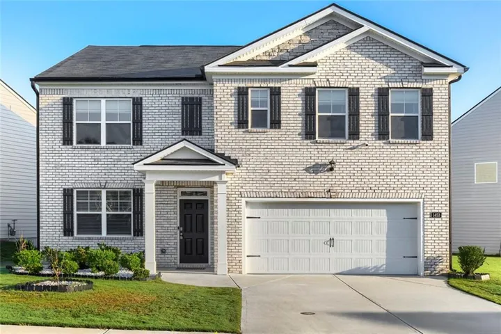 Two-story brick exterior, covered entry, black paneled front door, attached two-car garage, and a concrete driveway