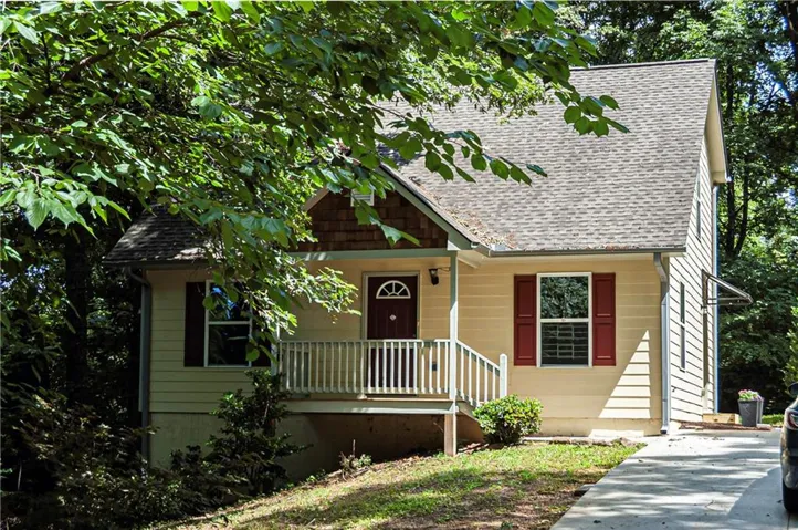 A-frame style residence featuring a front porch with white railing, a dark paneled entry door with an arched window, and red window shutters