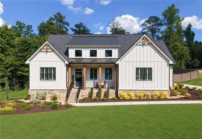 White board and batten siding, dark framed windows, stone foundation, covered front porch with wood columns, and dark metal roof accents