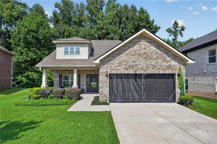 Brick facade, covered front entry, dormer window, attached two-car garage, and established landscaping