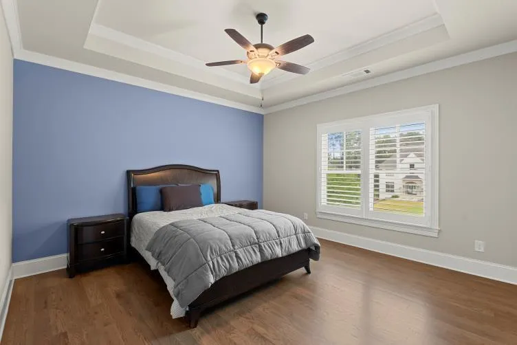Bedroom featuring dark wood-type flooring, ornamental molding, ceiling fan, and a raised ceiling