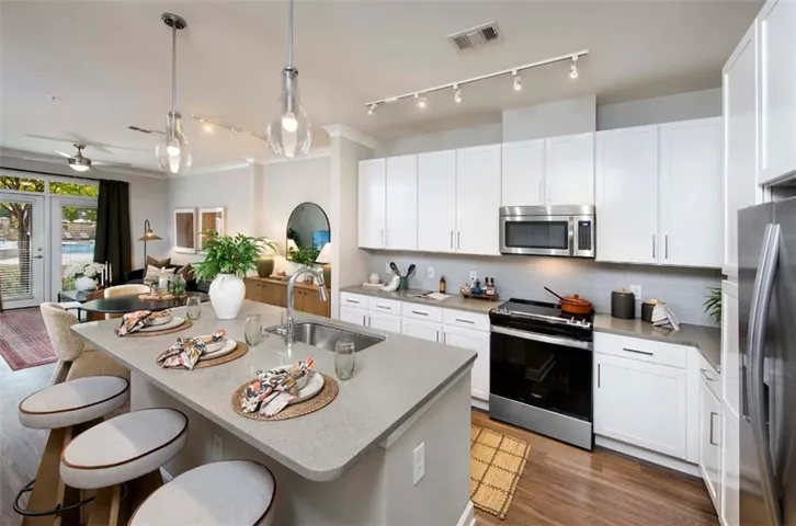 Kitchen with stainless steel appliances, white cabinetry, track lighting, a breakfast bar, and an island with sink