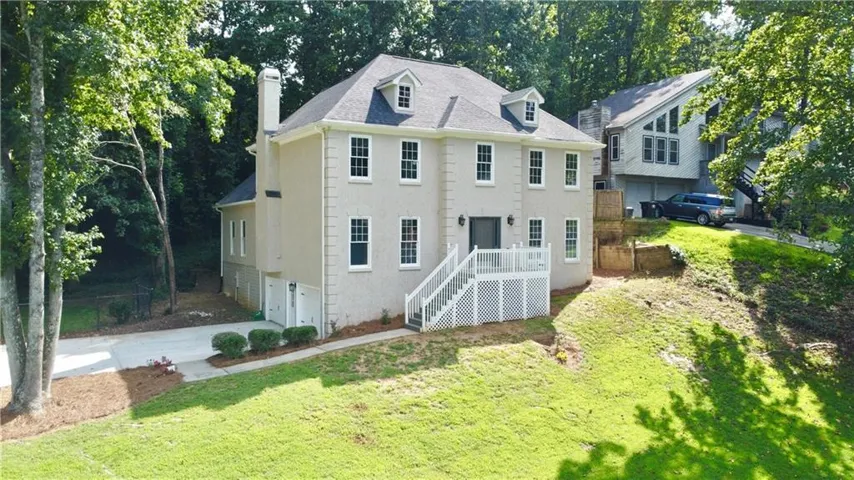 Two-story stucco exterior with dormer windows, a front deck with white railings, and a side-entry garage