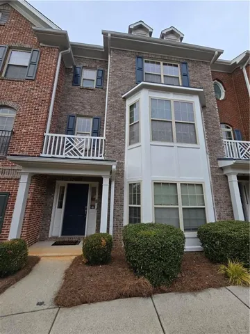 Brick exterior townhome featuring a projecting bay window, white-railed balcony, and dormer windows