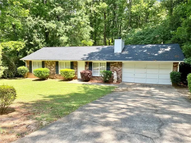Brick exterior ranch home featuring a two-car garage, mature landscaping, and a concrete driveway