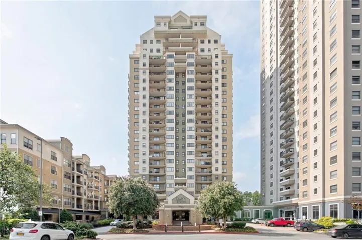 High-rise building with multiple balconies, a covered main entrance, and decorative landscaping