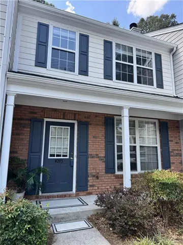 Brick and siding exterior with dark shutters, covered entry with white columns, and mature landscaping