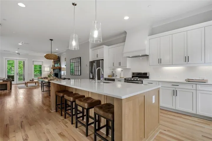 Contemporary kitchen featuring a large central island with seating, white shaker cabinetry, stainless steel appliances, and wood-finish flooring