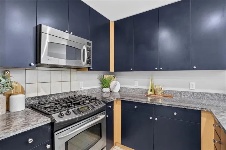 Kitchen featuring dark cabinetry, stainless steel range, built-in microwave, and stone-finish countertops