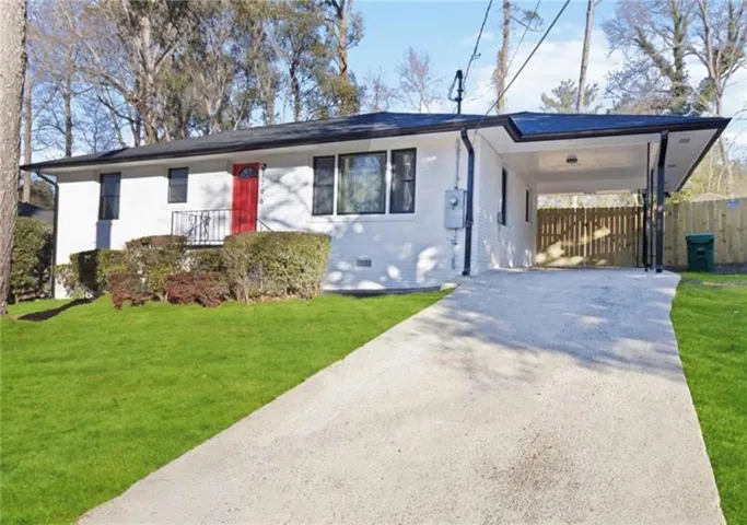 White exterior with black trim, red entry door, covered carport, concrete driveway, and front yard landscaping