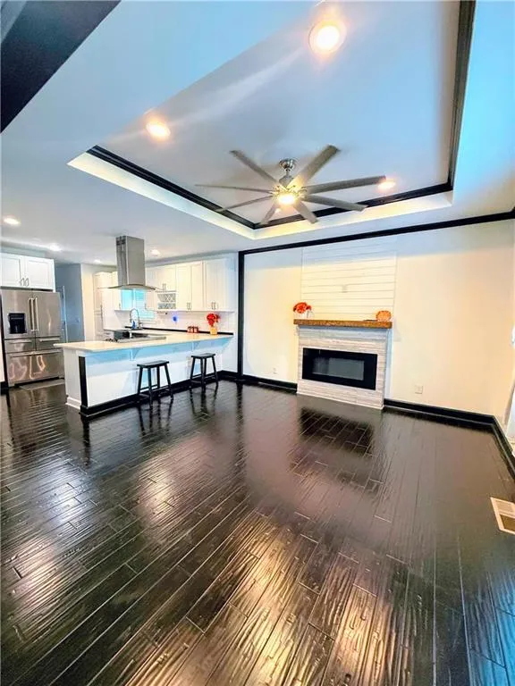 Living room with a tray ceiling, baseboards, ceiling fan, recessed lighting, and dark wood finished floors