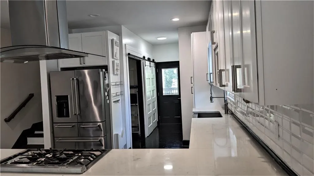 Kitchen with sink, appliances with stainless steel finishes, island exhaust hood, a barn door, and white cabinets