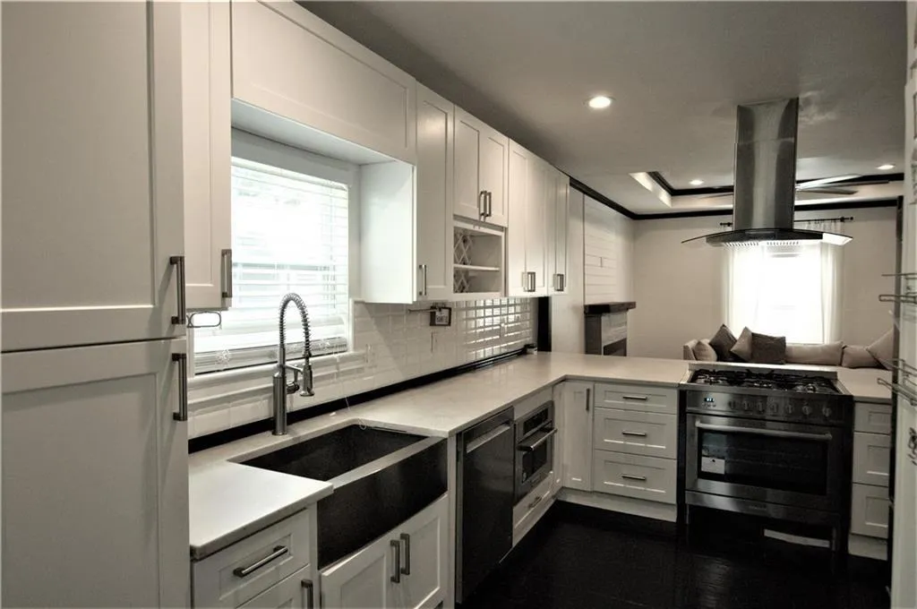 Kitchen featuring appliances with stainless steel finishes, island range hood, sink, white cabinets, and backsplash