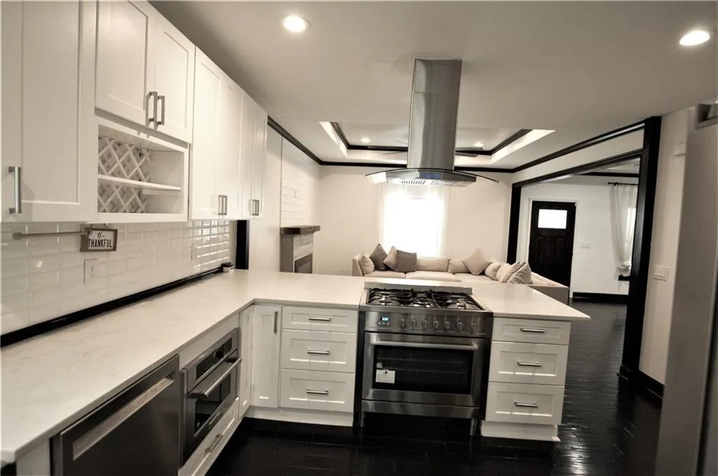 Kitchen featuring island exhaust hood, kitchen peninsula, white cabinets, and appliances with stainless steel finishes