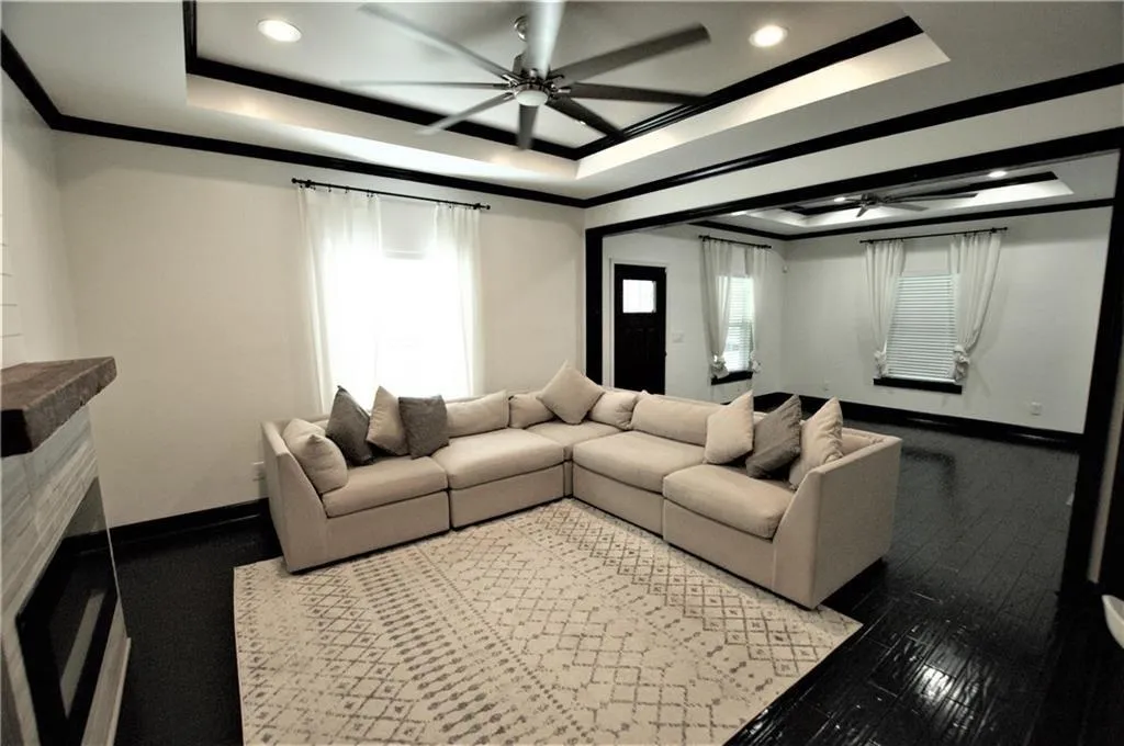 Living room with ceiling fan, ornamental molding, a raised ceiling, and wood-type flooring