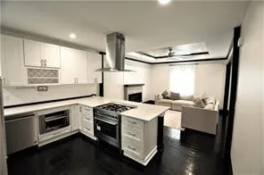 Kitchen with stainless steel range with gas cooktop, kitchen peninsula, wall oven, range hood, and white cabinets