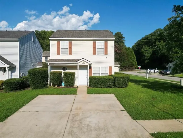 Two-story residence featuring light-colored siding, a front entry, concrete driveway, and established front landscaping